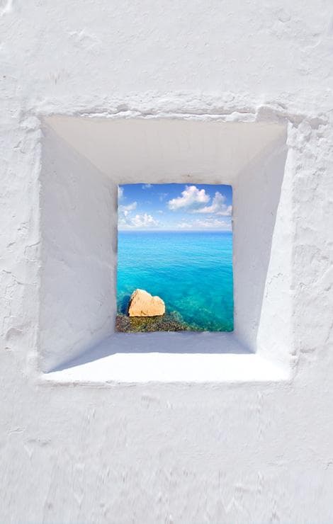 Vista sul mare turchese attraverso una finestra bianca in stile mediterraneo.