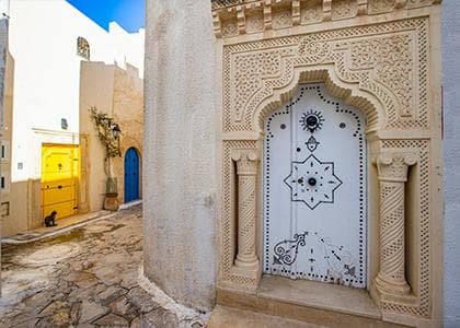 Traditional Tunisian architecture with a carved white door, a cobbled alley and white buildings in Hammamet